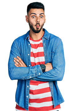 Young hispanic man with beard with arms crossed gesture making fish face with mouth and squinting eyes, crazy and comical.