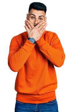 Young hispanic man with beard wearing casual orange sweater shocked covering mouth with hands for mistake. secret concept.