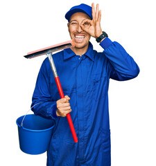 Bald man with beard wearing glass cleaner uniform and squeegee smiling happy doing ok sign with...