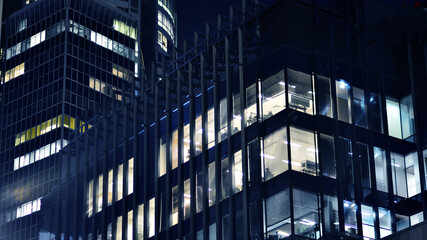 The glass facades of a modern skyscrapers at night. Modern glass office in city. Big glowing windows in modern offices buildings at night. In rows of windows light shines.