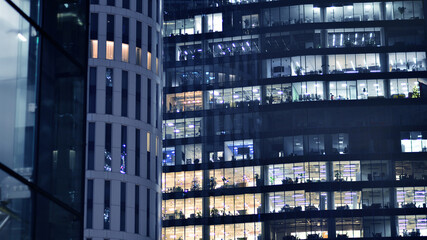 Fototapeta premium The glass facades of a modern skyscrapers at night. Modern glass office in city. Big glowing windows in modern offices buildings at night. In rows of windows light shines.