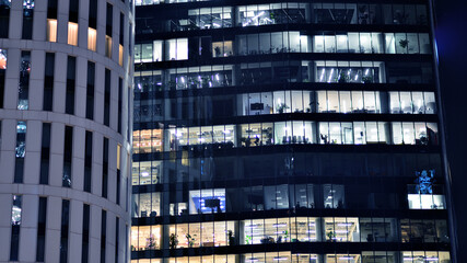 Fototapeta na wymiar The glass facades of a modern skyscrapers at night. Modern glass office in city. Big glowing windows in modern offices buildings at night. In rows of windows light shines.