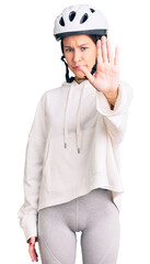 Beautiful brunette young woman wearing bike helmet and sporty clothes doing stop sing with palm of the hand. warning expression with negative and serious gesture on the face.