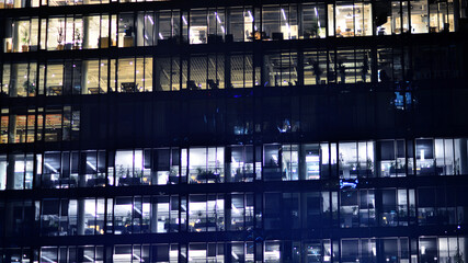 Fragment of the glass facade of a modern corporate building at night. Modern glass office  in city. Big glowing windows in modern office buildings at night, in rows of windows light shines. 