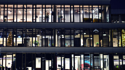 Fragment of the glass facade of a modern corporate building at night. Modern glass office  in city. Big glowing windows in modern office buildings at night, in rows of windows light shines. 