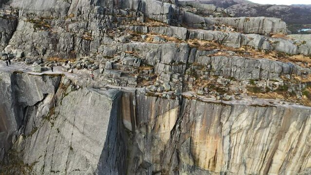 Areal shot of a couple standing at the edge of Preikestolen. First morning sunbeams reach the cliff formation. Massive rocks surrounding the couple. Dangerous place for a hike. Beauty of the nature