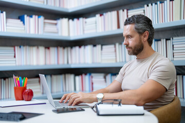 Teacher with laptop in library classroom. Handsome teacher work on laptop in university library....