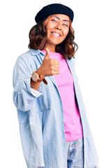 Young beautiful mixed race woman wearing french look with beret doing happy thumbs up gesture with hand. approving expression looking at the camera showing success.