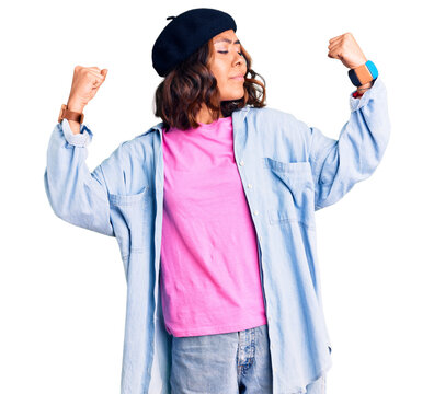 Young beautiful mixed race woman wearing french look with beret showing arms muscles smiling proud. fitness concept.