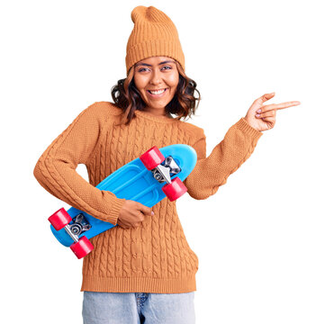 Young beautiful mixed race woman holding skate smiling happy pointing with hand and finger to the side