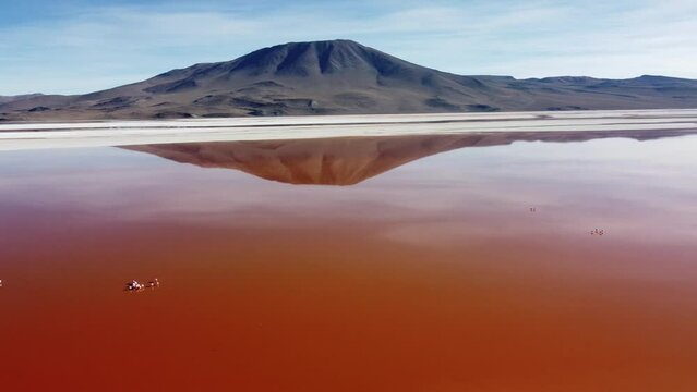Camera approaching and rises up to the Perfect reflection of a cone-shaped mountain on the red water of Laguna Colorado Bolivia creating a duplicate image