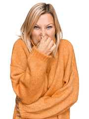 Middle age caucasian woman wearing casual winter sweater smelling something stinky and disgusting, intolerable smell, holding breath with fingers on nose. bad smell