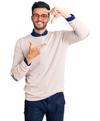 Young handsome hispanic man wearing elegant clothes and glasses smiling making frame with hands and fingers with happy face. creativity and photography concept.