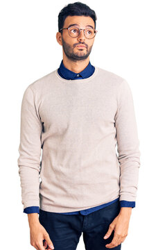 Young handsome hispanic man wearing elegant clothes and glasses smiling looking to the side and staring away thinking.