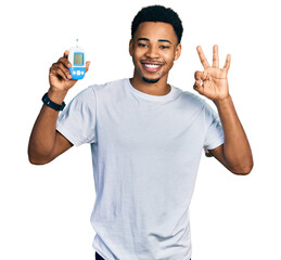 Young african american man holding glucometer device doing ok sign with fingers, smiling friendly gesturing excellent symbol