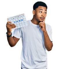 Young african american man holding rainy weather calendar serious face thinking about question with...