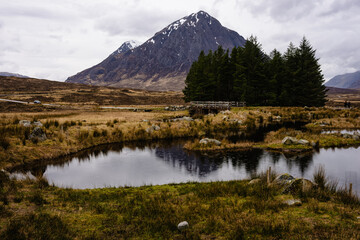 Beautiful gloomy Buachaille Etive Mor Mountain vista with river, pond, and trees in Glencoe, the Scottish Highlands, Scotland UK