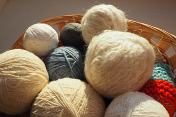 White, beige and blue woolen and acrylic threads wound into a ball or skein. Several skeins of light yarn in a basket. Knitting as a hobby. A clew of thread.