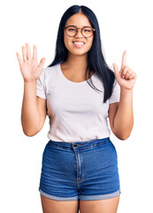 Young beautiful asian girl wearing casual clothes and glasses showing and pointing up with fingers number seven while smiling confident and happy.