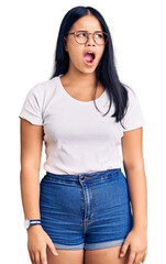 Obraz premium Young beautiful asian girl wearing casual clothes and glasses angry and mad screaming frustrated and furious, shouting with anger. rage and aggressive concept.
