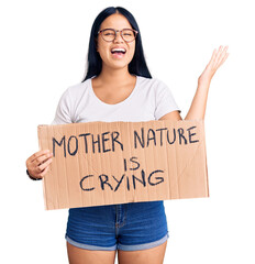 Young beautiful asian girl holding mother nature is crying protest cardboard banner celebrating victory with happy smile and winner expression with raised hands