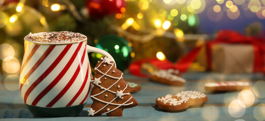 Cup of hot chocolate and gingerbread cookies on wooden table against blurred lights