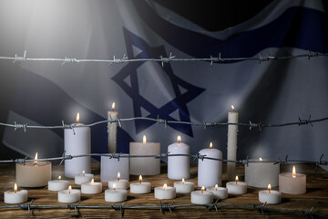 Barbed wire and burning candles on table against flag of Israel. International Holocaust...