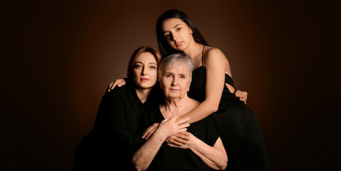 Portrait of mature woman with her adult daughter and mother on dark brown background