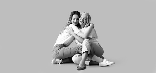 Black and white portrait of sitting young woman and her mother on grey background