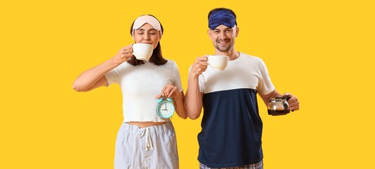 Young couple with coffee and alarm clock on yellow background