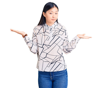 Young beautiful chinese woman wearing casual shirt clueless and confused expression with arms and hands raised. doubt concept.