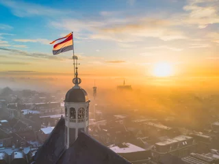 Foto op Canvas Drone view across town of Sneek with Dutch flag on top of a church at sunrise © Thomas