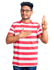 Handsome latin american young man wearing casual clothes and glasses smiling swearing with hand on chest and fingers up, making a loyalty promise oath