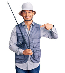 Handsome latin american young man wearing fisherman equipment pointing finger to one self smiling...