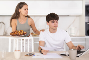 Young woman offering pie to young guy working on laptop in kitchen at home