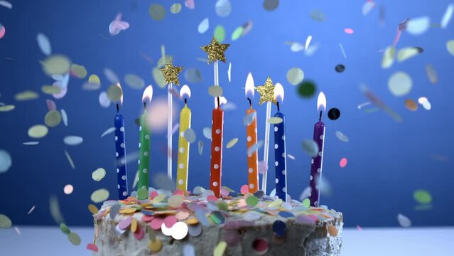 Candles on birthday cake with confetti falling in super slow-motion at 1000 fps on blue backdrop
