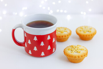 red cup with fir trees and mini cakes with snowflake on table