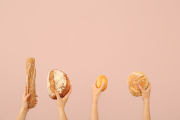 Female hands holding loaves of different fresh bread on pink background