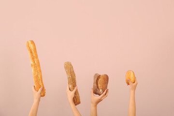 Female hands holding loaves of different fresh bread on pink background