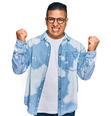 Young latin man wearing casual clothes and glasses screaming proud, celebrating victory and success very excited with raised arms