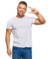 Handsome muscle man wearing casual white tshirt smiling and confident gesturing with hand doing small size sign with fingers looking and the camera. measure concept.