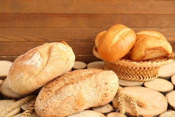 Loaves of fresh bread with wheat spikelets on wooden background