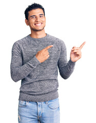 Hispanic handsome young man wearing casual sweater smiling and looking at the camera pointing with two hands and fingers to the side. - obrazy, fototapety, plakaty