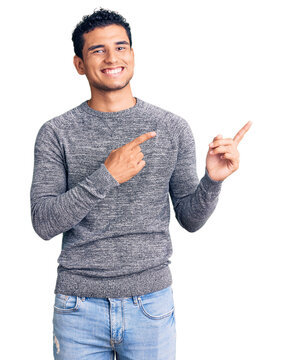 Hispanic handsome young man wearing casual sweater smiling and looking at the camera pointing with two hands and fingers to the side.