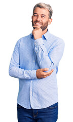 Young handsome blond man wearing elegant shirt looking confident at the camera smiling with crossed arms and hand raised on chin. thinking positive.