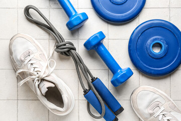 Barbell plates, shoes, skipping rope and dumbbells on white tile background