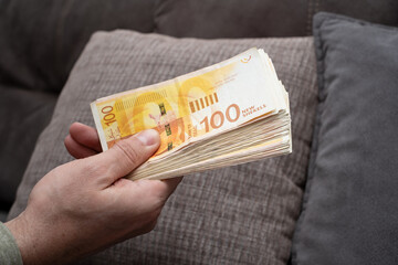 A bunch of Israeli New Shekels (NIS) money banknotes in nominal 100 nis. Men hold shekels on hand....