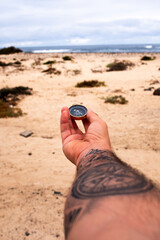 Travel adventure lifestyle concept with man holding navigation compass in front of dramatic sky and ocean landscape. Journey and destination. Lost direction and life. People finding the way