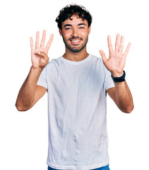 Hispanic young man with beard wearing casual white t shirt showing and pointing up with fingers number nine while smiling confident and happy.