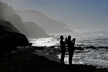 Silhouette of couple photographing surf, sea and coast using mobile devices, Searose Beach Oregon 